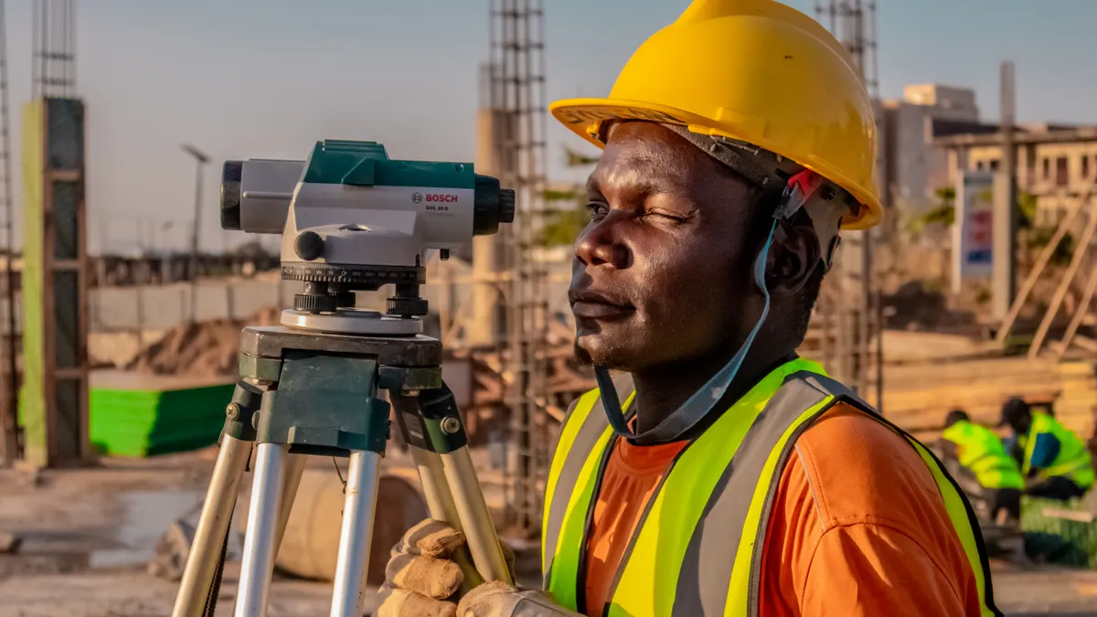 Surveyor beside a tripod-mounted instrument at a job site